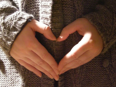 Image: the hands of someone wearing a sweater form the shape of a heart