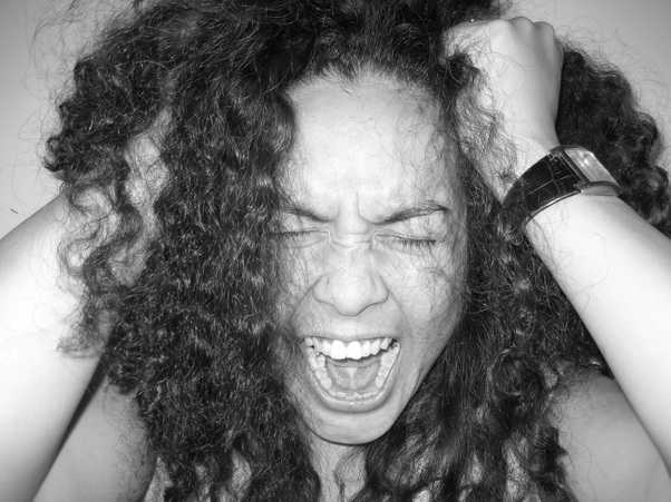 Image: a woman with curly hair pulling her hair and screaming with her eyes shut