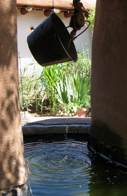 Image: a bucket of water hangs above and drips into a well