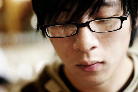 Image: a young adult with glasses and black hair looks downward sadly