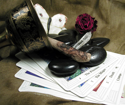 Image: a goblet on its side with rocks,a  flower, and a butterfly spilling out of it, with tarot cards underneath.